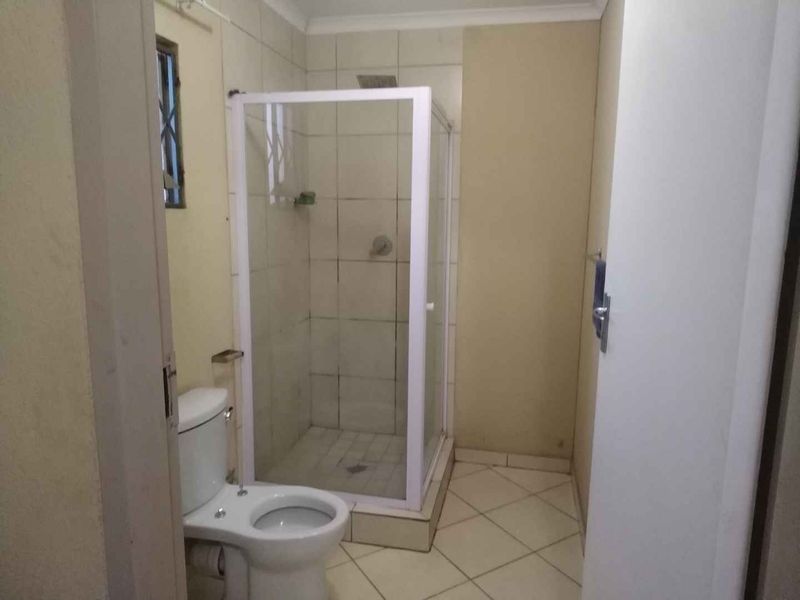 A functional bathroom featuring a corner shower enclosure, toilet, and neutral wall and floor tiling.