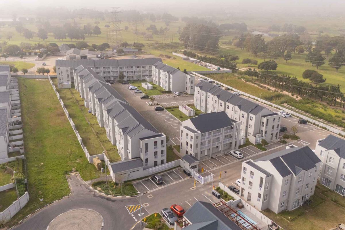 Aerial view of a modern residential apartment complex featuring multiple multi-story buildings, paved parking areas, and secure gated access.
