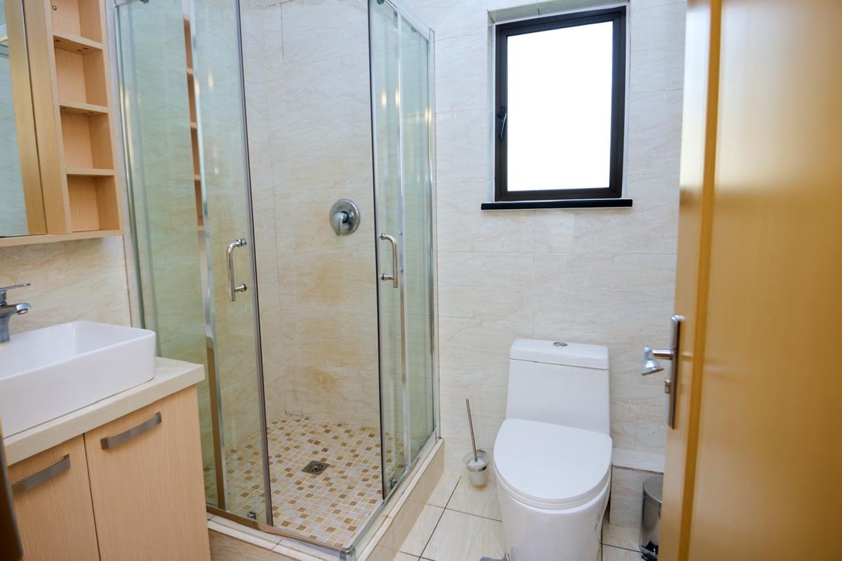 A functional bathroom featuring a glass shower enclosure, modern vanity with vessel sink, toilet, and neutral tiled finishes.