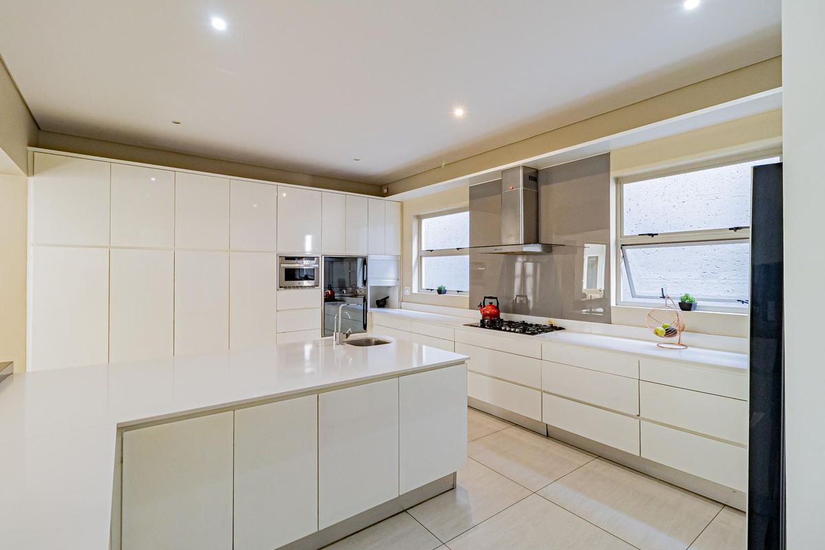 Modern kitchen featuring high-gloss cabinetry, a central island with a sink, stone countertops, a built-in oven, and a stainless steel extractor fan.