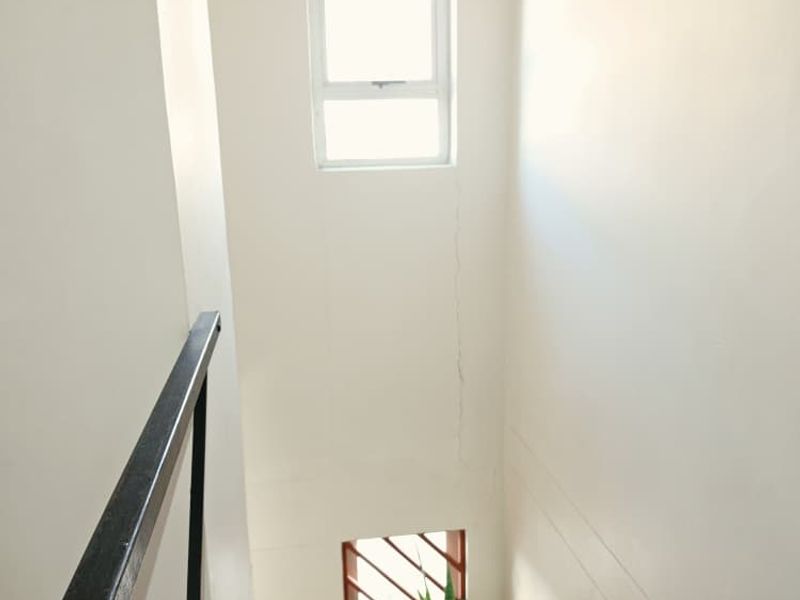 A vertical view of a stairwell area featuring a metal railing and windows with security bars, showing visible wall cracking.
