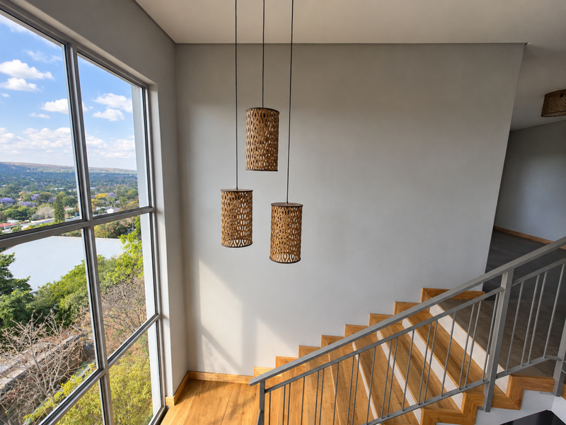 A bright, modern staircase landing featuring timber stairs, a sleek metal balustrade, and large windows offering expansive elevated views.