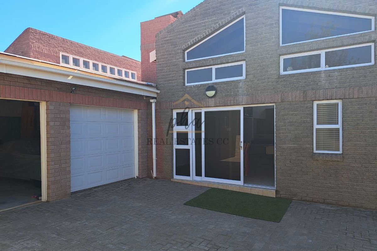 Rear exterior view of the property featuring a brick facade, paved driveway, garage access, and large sliding glass doors.