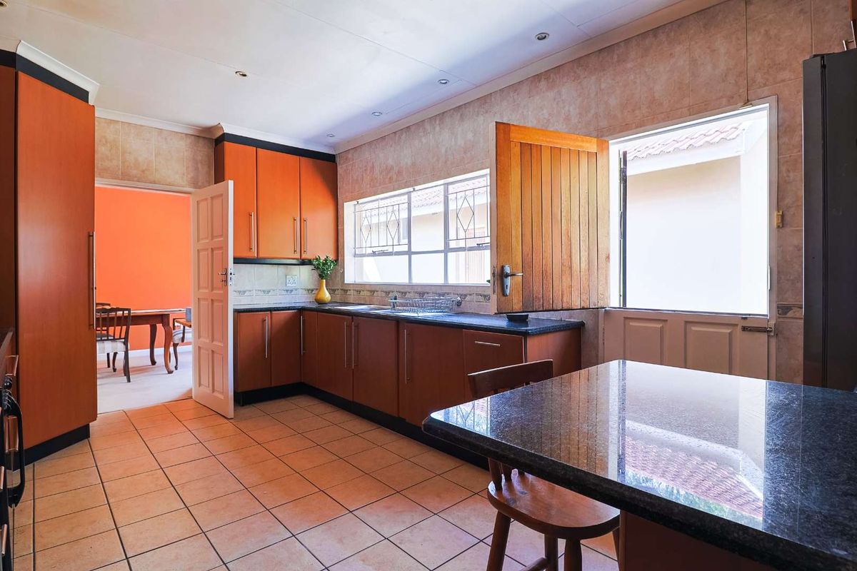 A functional kitchen featuring wooden cabinetry, dark granite countertops, tiled flooring, and a stable-style door providing direct access to the exterior.