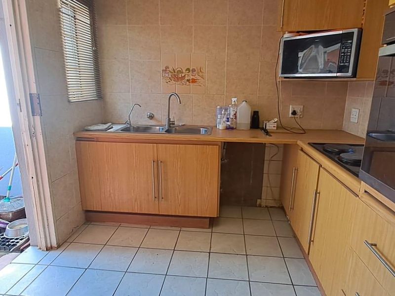 A dated kitchen featuring laminate cabinetry, built-in oven, hob, and double bowl sink, with direct access to an outdoor area.