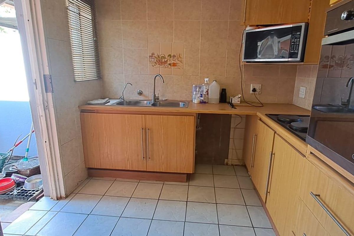 A dated kitchen featuring laminate cabinetry, built-in oven, hob, and double bowl sink, with direct access to an outdoor area.