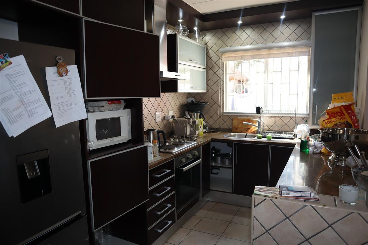 A functional kitchen featuring dark cabinetry, built-in oven and hob, stainless steel sink, and tiled backsplash with natural light from the window.