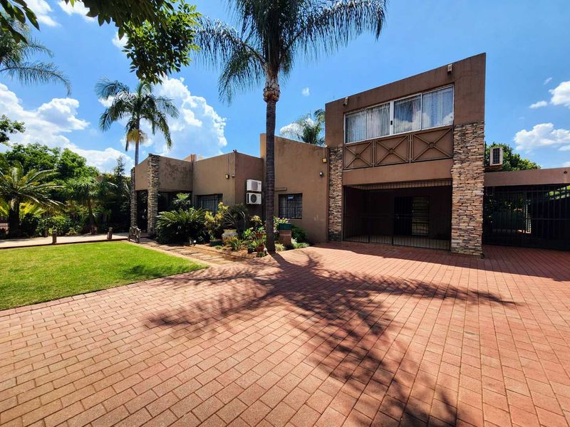 Front exterior view of the house featuring a paved driveway, stone-clad facade, and a well-maintained garden with mature palm trees.