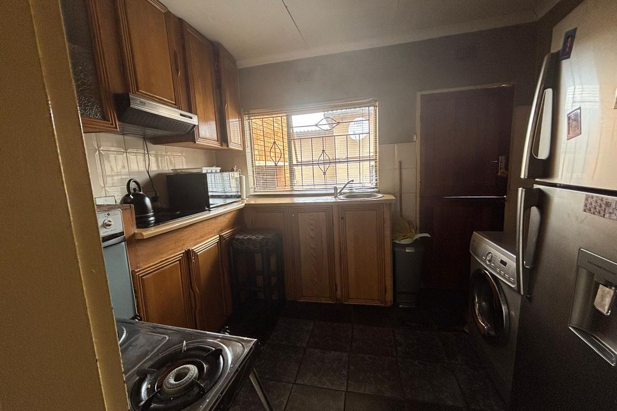 A compact, dated kitchen featuring wooden cabinetry, tiled flooring, and a window overlooking the exterior, providing functional space for meal preparation.