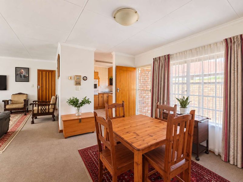 Open plan living and dining area featuring carpeted flooring, timber doors, and access to a functional kitchen space with neutral finishes.