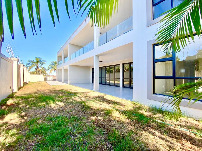 Rear view of the apartment building featuring a covered patio, glass balustrades, large sliding doors, and a private garden area with perimeter security fencing.