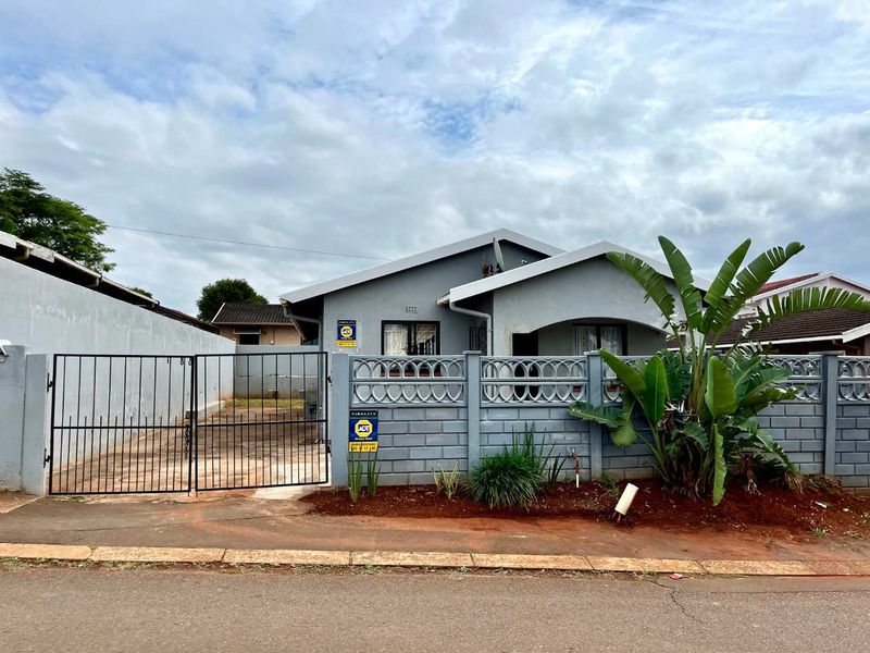 Front view of a single-story house featuring a perimeter wall, metal driveway gate, and paved parking area.