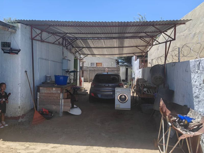 An open-sided carport or garage area featuring a corrugated metal roof, steel support structure, and perimeter walling with security fencing.