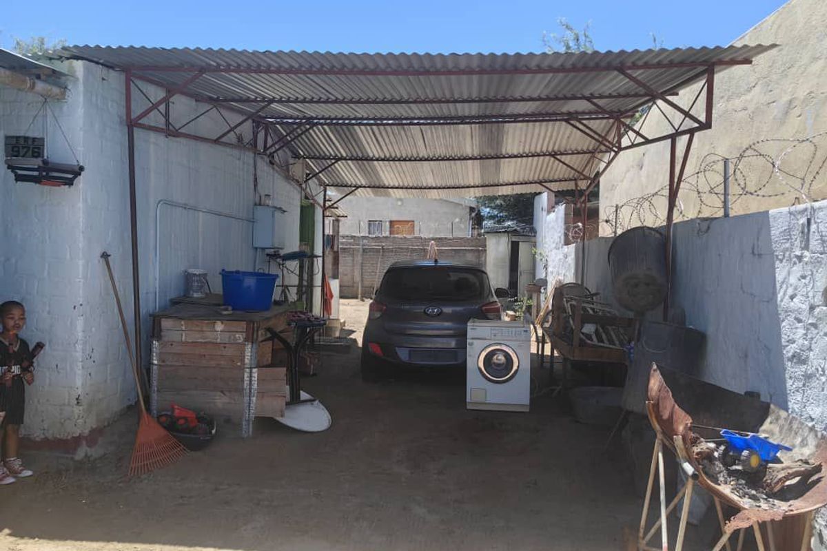 An open-sided carport or garage area featuring a corrugated metal roof, steel support structure, and perimeter walling with security fencing.