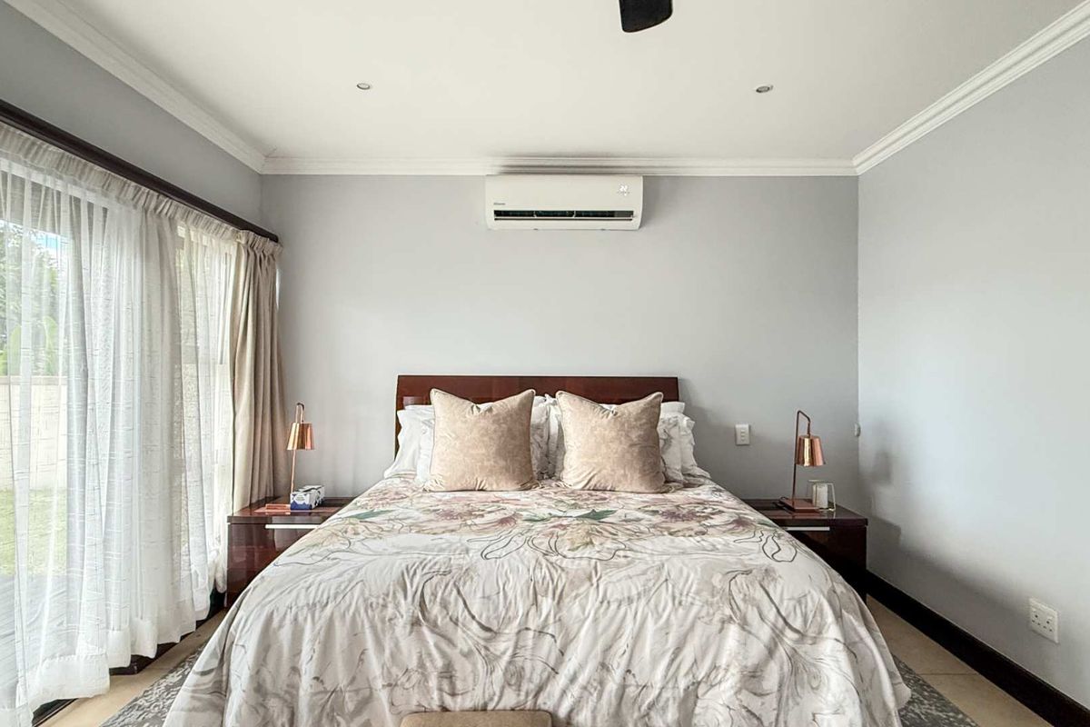 A well-maintained bedroom featuring a wall-mounted air conditioning unit, recessed ceiling lighting, and large sliding glass doors providing access to the garden.