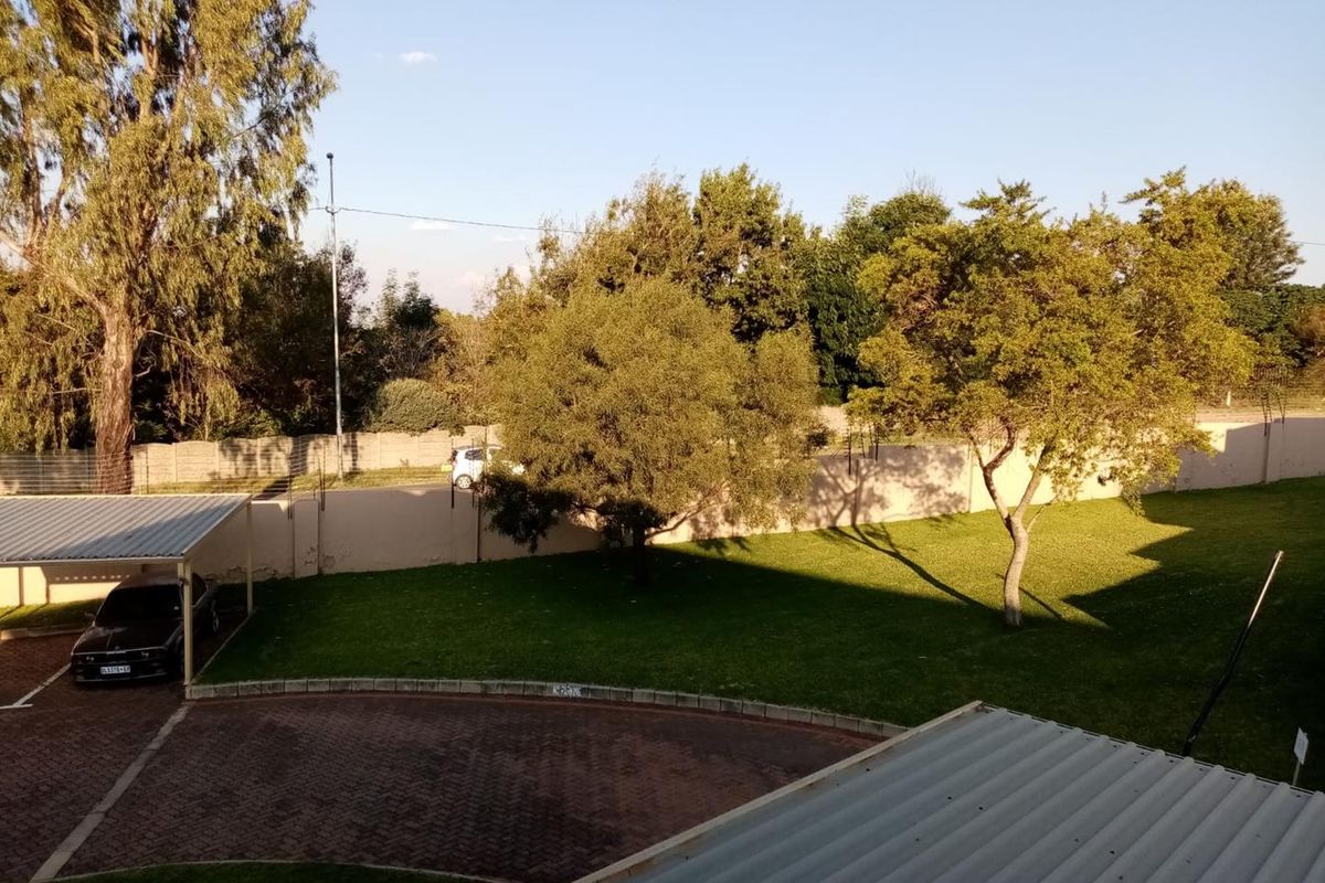 An elevated view of the apartment complex grounds featuring a paved driveway, covered carport, and a well-maintained lawn area.