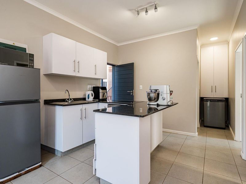 Modern kitchen featuring white cabinetry, granite countertops, a central island, tiled flooring, and a convenient built-in pantry cupboard for additional storage.