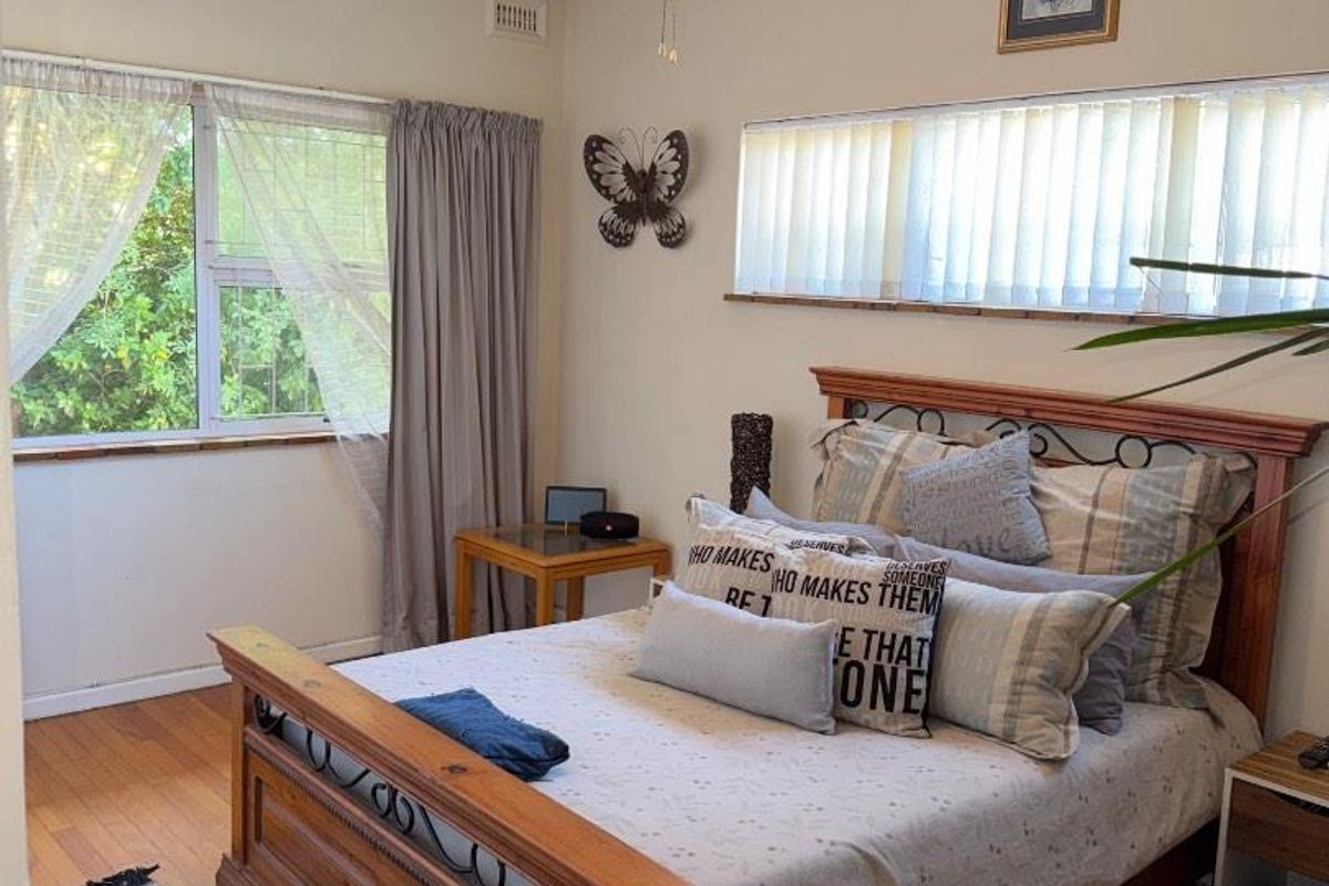 A well-lit bedroom featuring polished timber flooring, a ceiling fan, and dual-aspect windows providing natural light.