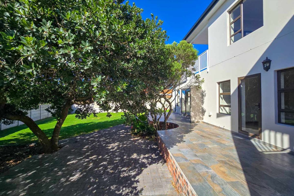A well-maintained rear exterior view featuring a paved patio area, landscaped garden, and access to the home via glass doors and windows.