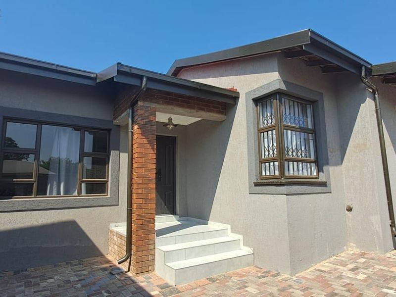 Front facade of the house featuring a brick pillar entrance, tiled steps, and modern aluminium window frames with security bars.