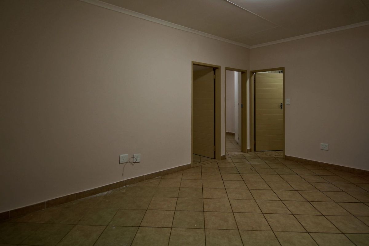 An empty living area featuring neutral wall tones, tiled flooring, and multiple internal doorways leading to other parts of the apartment.
