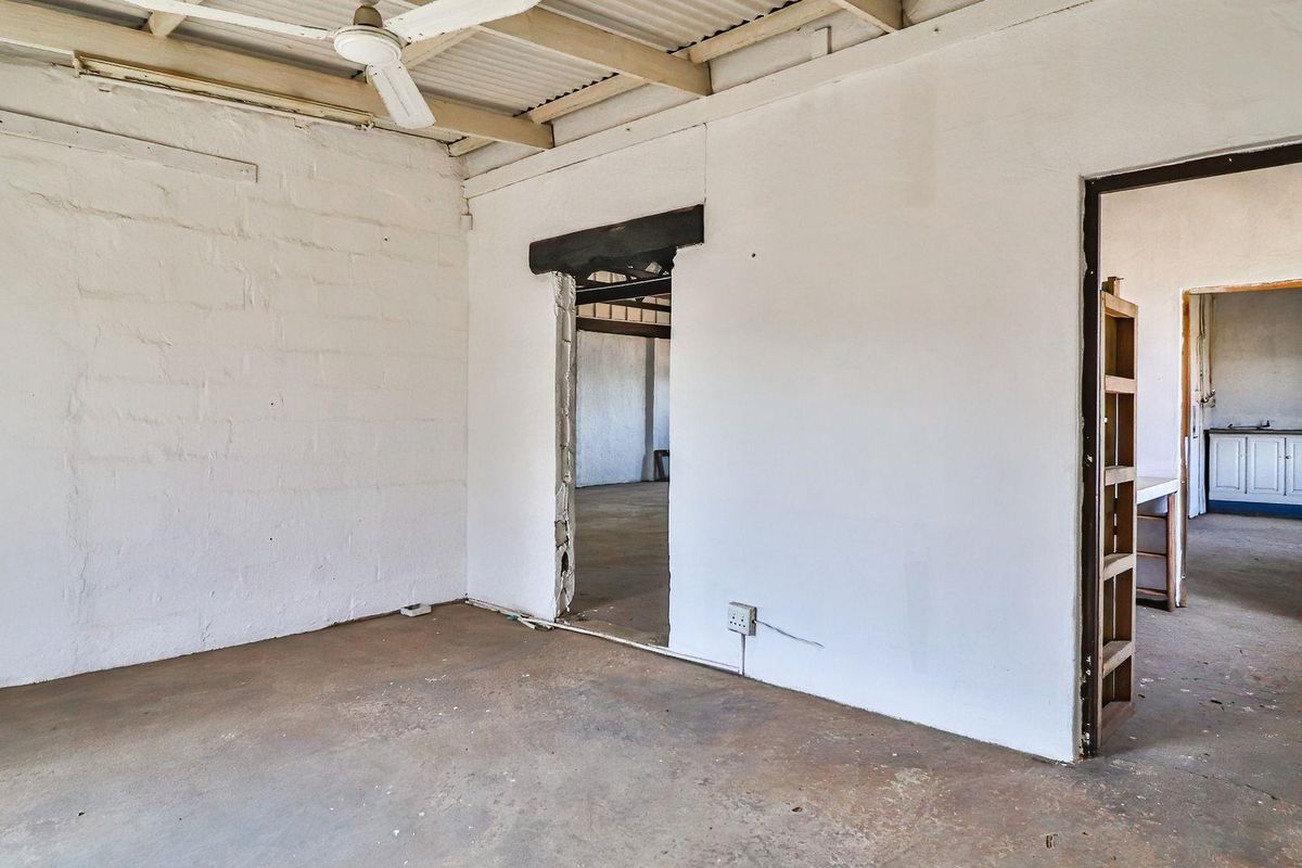 An empty, rustic living area featuring exposed beam ceilings, concrete floors, and an unfinished doorway leading to an adjacent room.