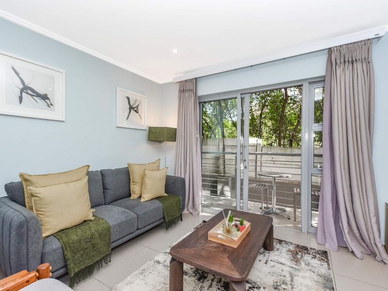 A bright and well-maintained living room featuring tiled floors, recessed lighting, and large sliding glass doors that provide access to an outdoor balcony area.
