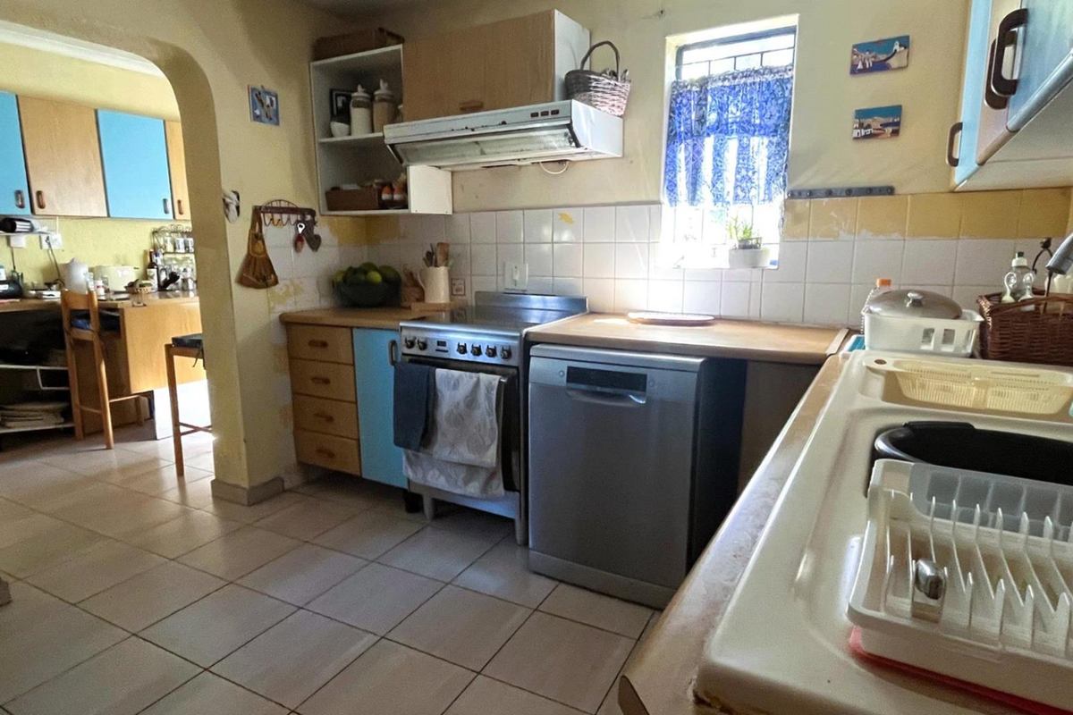 A dated kitchen featuring tiled flooring, built-in cabinetry, a double sink, and a tiled backsplash, offering potential for a modern renovation.