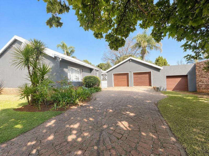 Front view of a well-maintained house featuring a paved driveway, landscaped garden, and a triple garage with roller shutter doors.