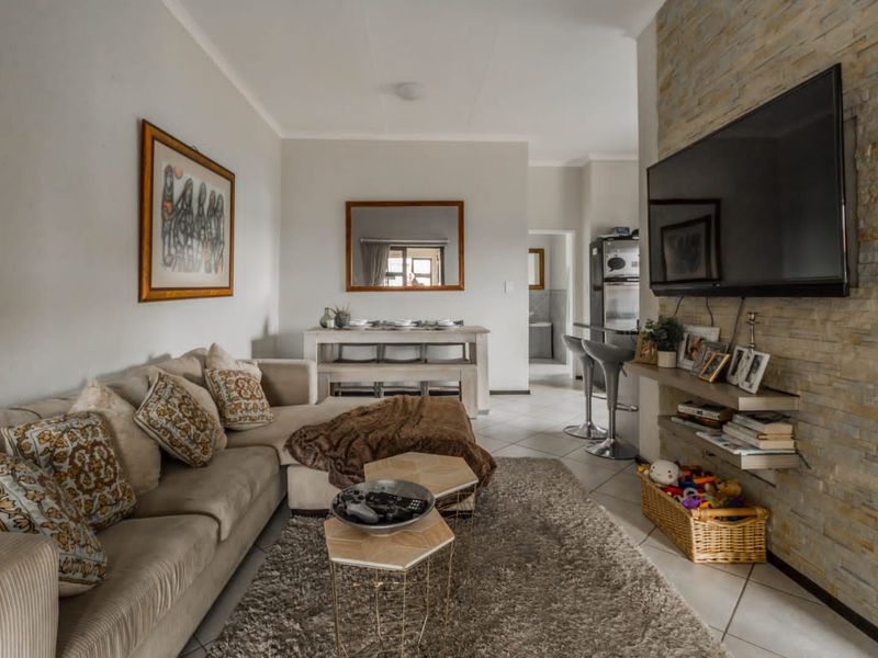 Open-plan living area featuring tiled flooring and a distinctive stone-clad feature wall, seamlessly connecting to the dining and kitchen spaces.