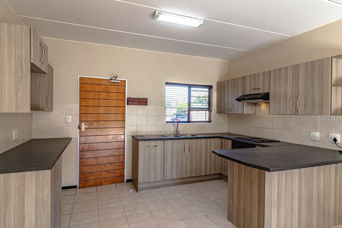 A functional kitchen featuring laminate cabinetry, dark countertops, a built-in hob with extractor fan, and tiled flooring.