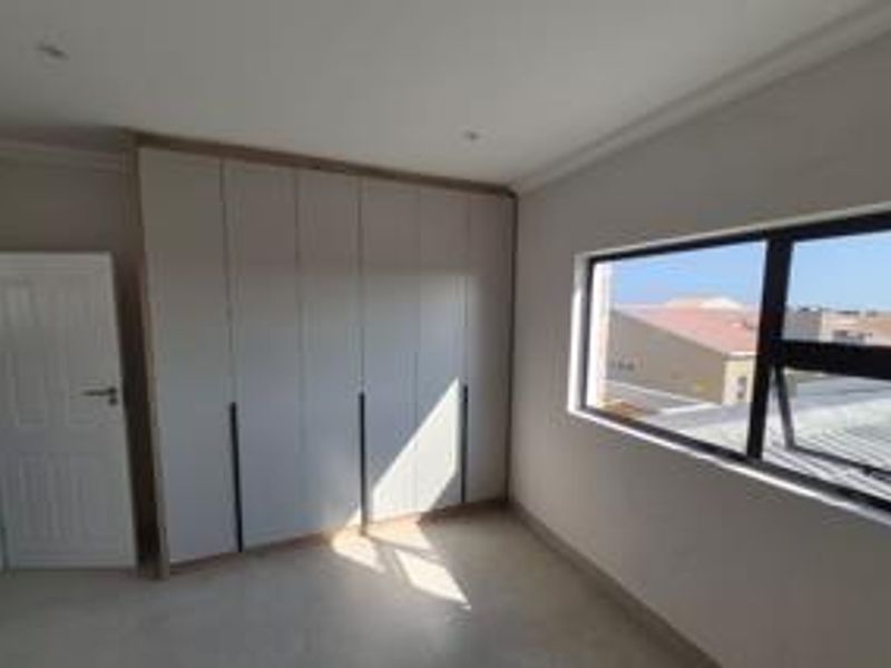 A bright, empty bedroom featuring modern built-in cupboards, recessed ceiling lighting, and large aluminium-framed windows.