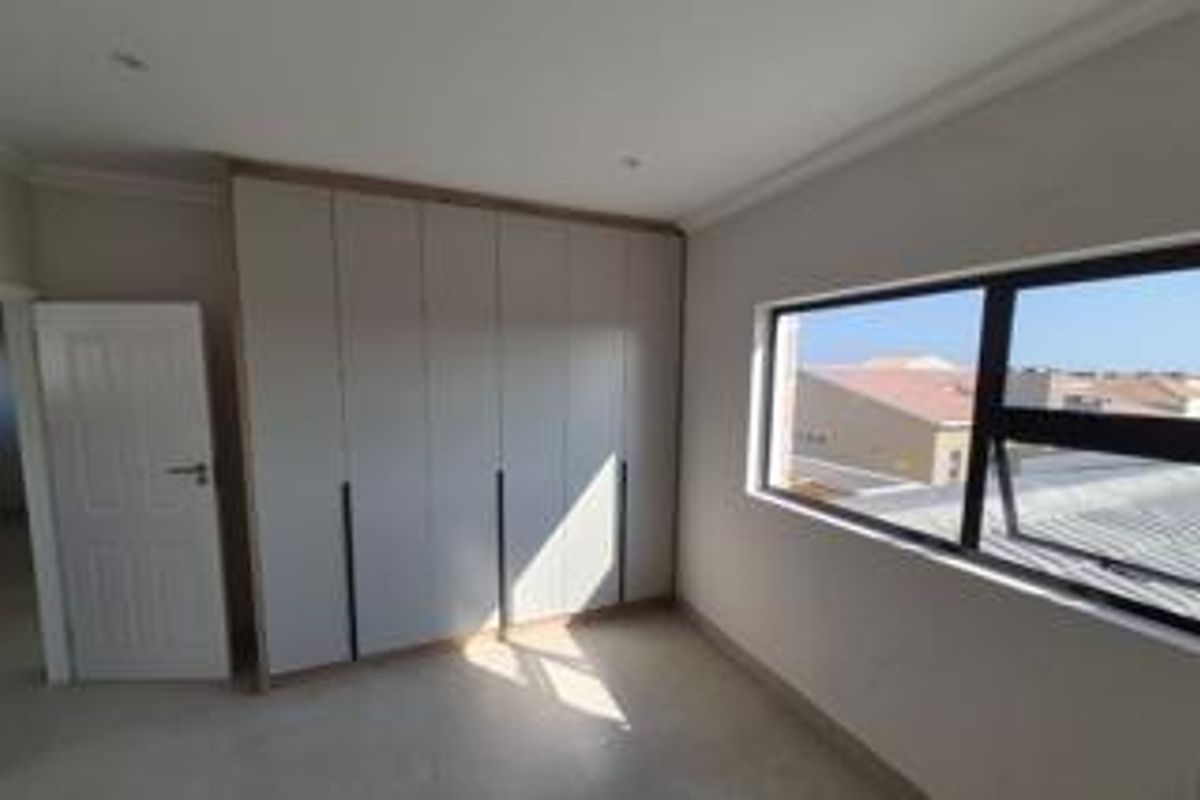 A bright, empty bedroom featuring modern built-in cupboards, recessed ceiling lighting, and large aluminium-framed windows.