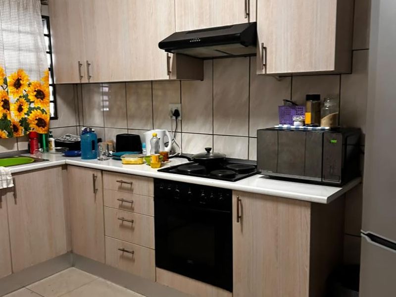 A functional kitchen featuring light wood-tone cabinetry, tiled splashbacks, integrated oven and hob, and tiled flooring.