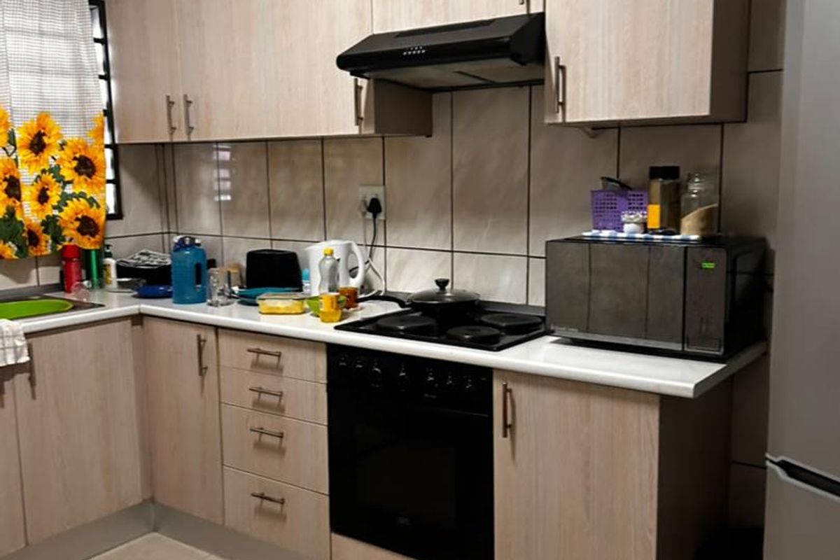 A functional kitchen featuring light wood-tone cabinetry, tiled splashbacks, integrated oven and hob, and tiled flooring.