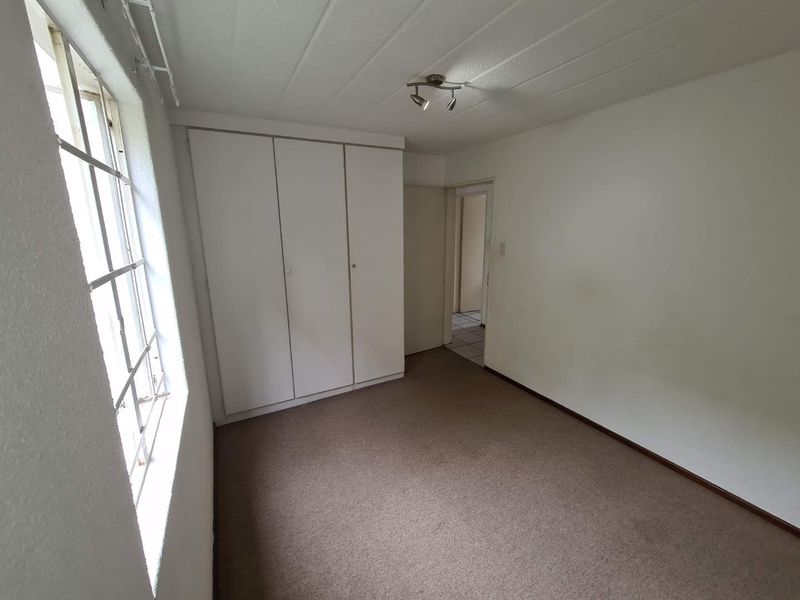 A vacant bedroom featuring built-in wardrobes, carpeted flooring, and a window, offering a blank canvas for personalization.
