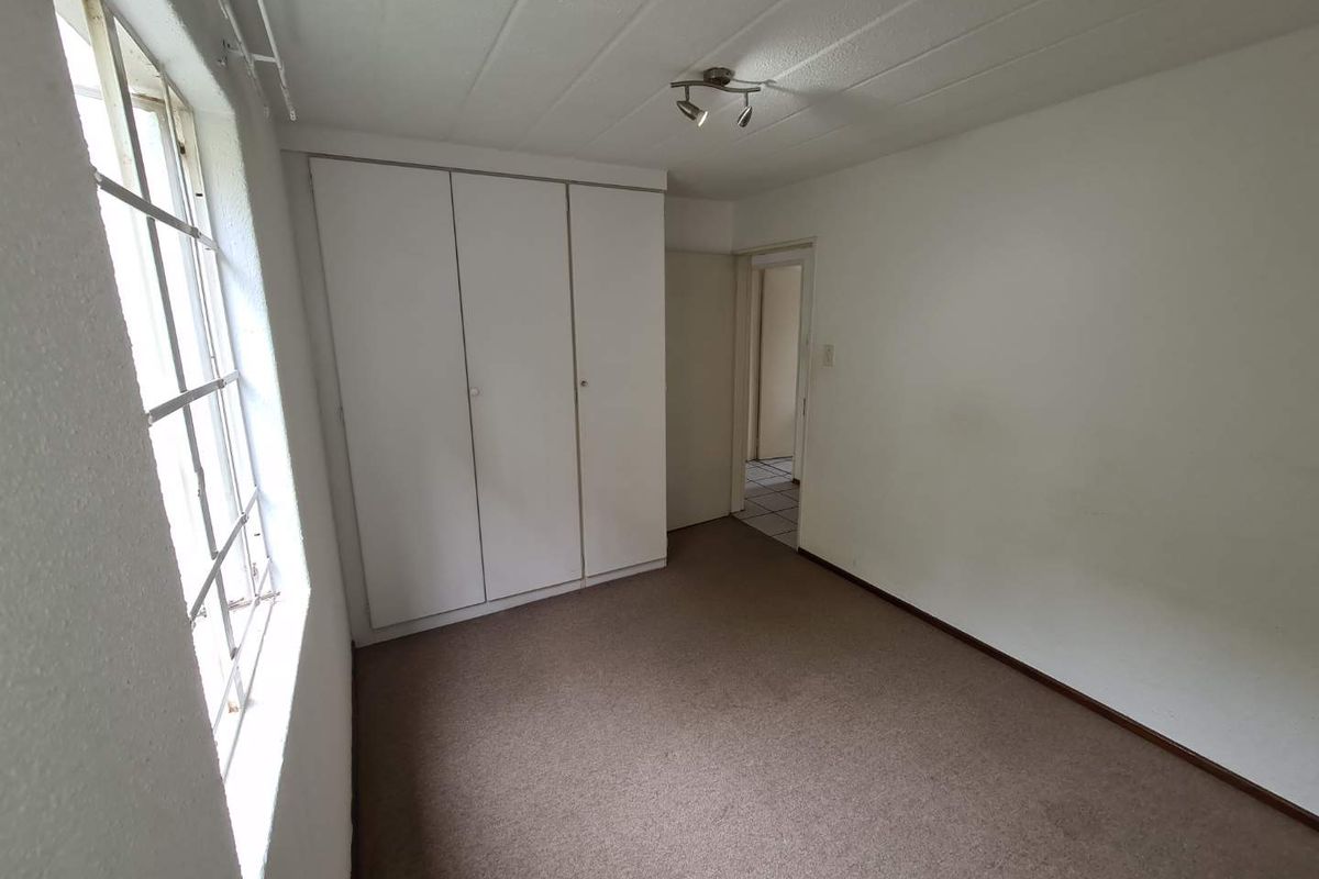 A vacant bedroom featuring built-in wardrobes, carpeted flooring, and a window, offering a blank canvas for personalization.