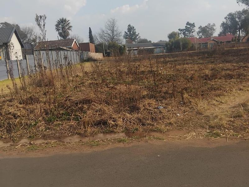 A vacant residential plot featuring level ground, boundary fencing, and direct access to a paved road in a developed neighborhood.