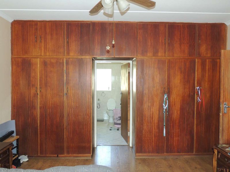 Bedroom featuring extensive floor-to-ceiling built-in wooden cupboards and a ceiling fan, with direct access to an en-suite bathroom.