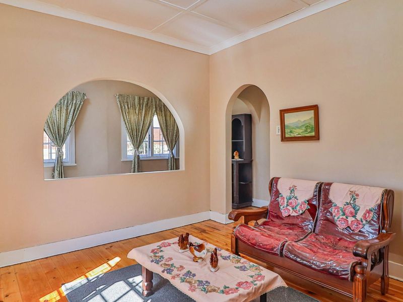 A living room featuring original hardwood flooring, coved ceilings, and distinctive arched architectural openings connecting to adjacent spaces.