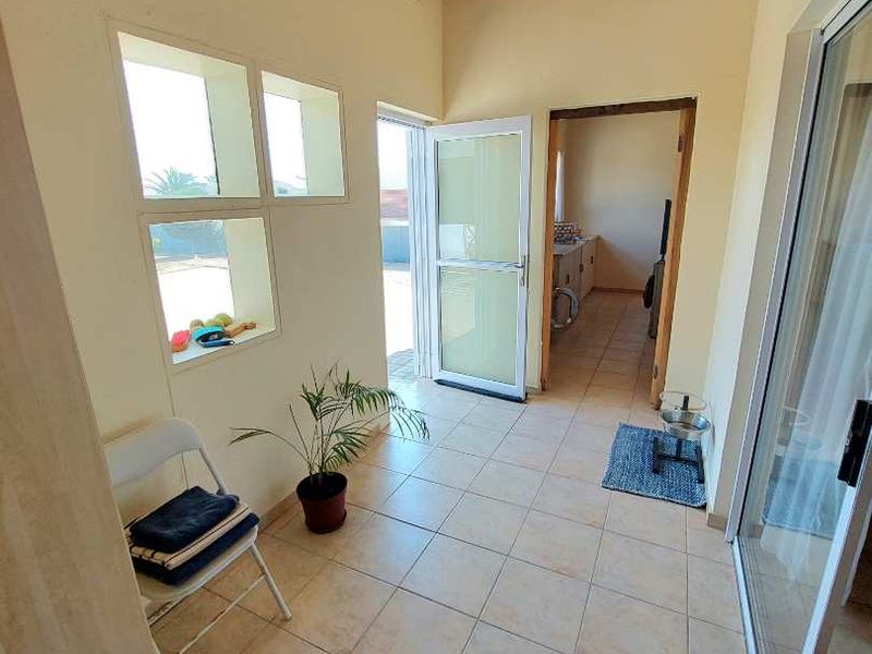 A bright hallway featuring tiled flooring and an exposed timber beam ceiling, providing access to adjacent rooms and outdoor areas.