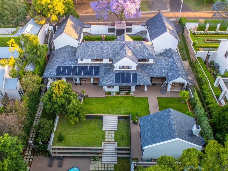 Aerial view of a well-maintained residential property featuring a slate roof, solar panels, a landscaped garden, and a swimming pool.
