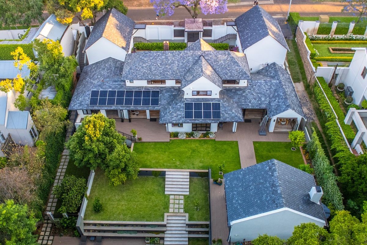 Aerial view of a well-maintained residential property featuring a slate roof, solar panels, a landscaped garden, and a swimming pool.