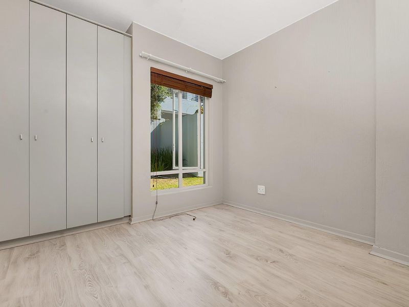 A bright, empty bedroom featuring light-toned laminate flooring, neutral walls, and floor-to-ceiling built-in cupboards with a window overlooking the exterior.