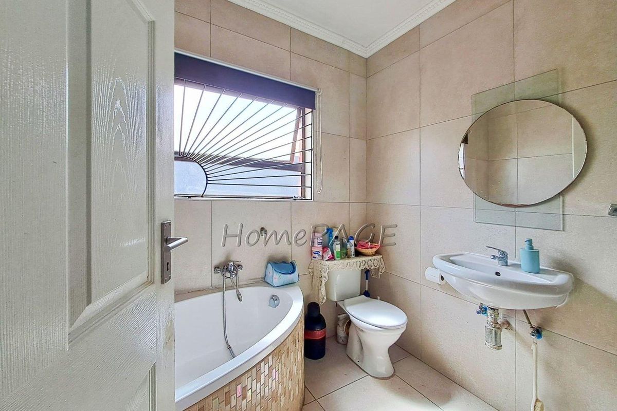 A functional bathroom featuring a corner bathtub with mosaic tiling, a wall-mounted basin, and a toilet, finished with neutral wall and floor tiles.
