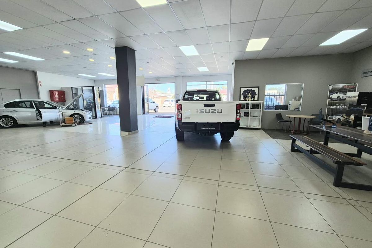 Spacious vehicle showroom or service area featuring tiled flooring, suspended ceiling with recessed lighting, and an open-plan layout suitable for automotive display.