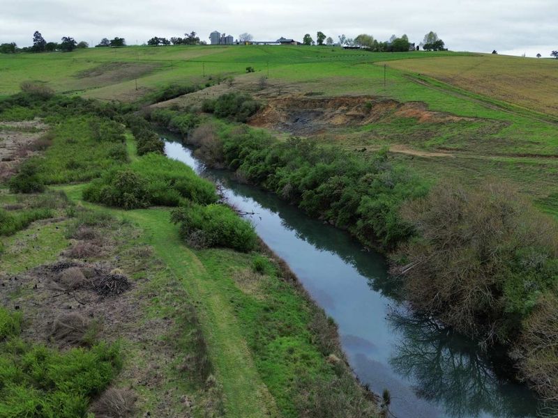 Aerial view of a rural property featuring a river running through open pasture land with visible natural vegetation and surrounding hills.