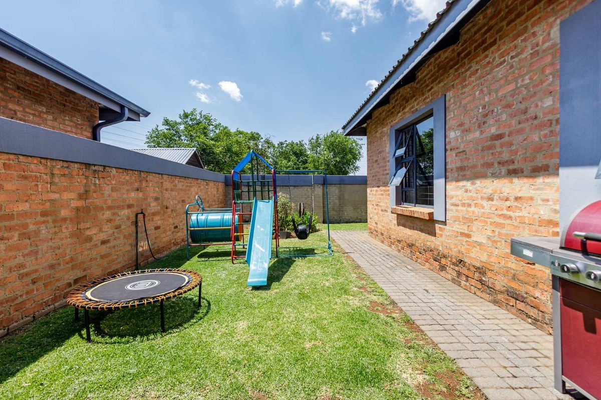 A private rear garden area featuring a paved walkway, exposed brick boundary walls, and a lawn space.
