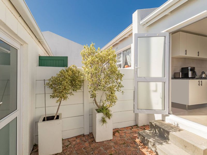 A neat rear courtyard featuring brick paving, concrete steps, and a white boundary wall, providing direct access to the kitchen area.