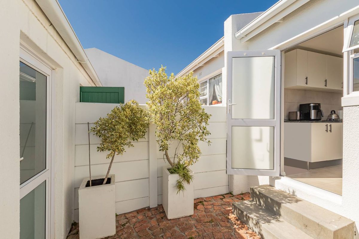 A neat rear courtyard featuring brick paving, concrete steps, and a white boundary wall, providing direct access to the kitchen area.